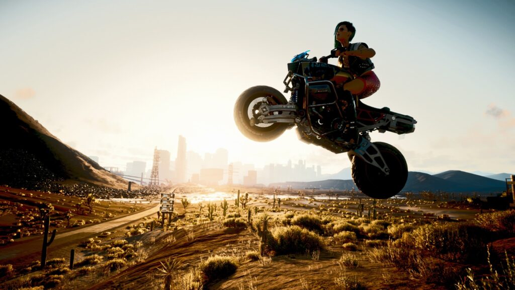Motorradfahrerin springt durch die Luft in der Wüste vor Night City. Im Hintergrund die Stadt bei Sonnenuntergang. Screenshot aus dem Spiel Cyberpunk 2077 im Blog von Nastja der Mox.