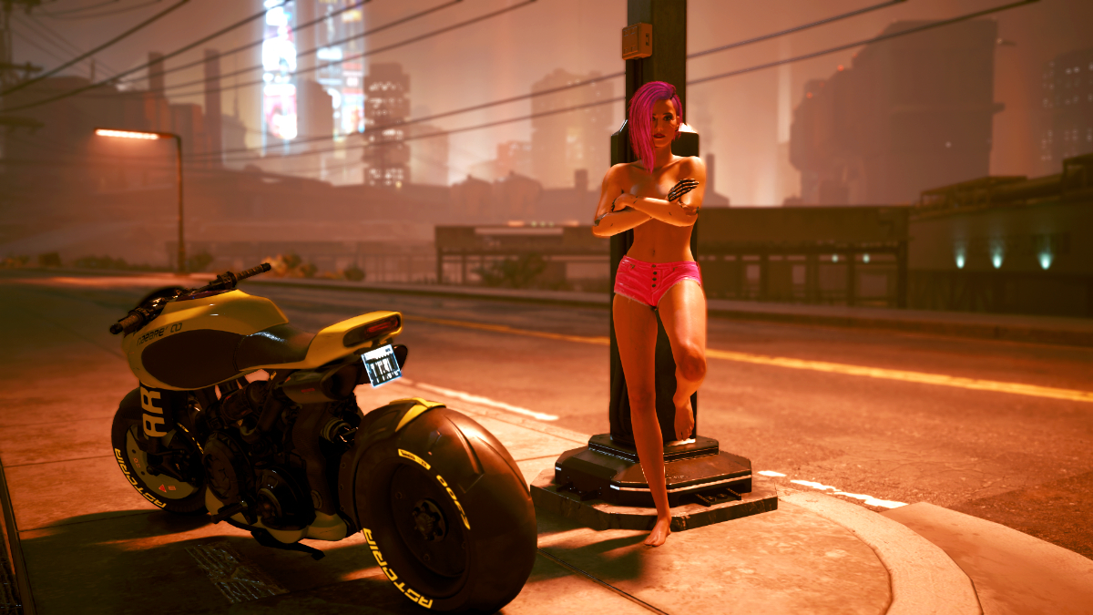 Frau nur mit Shorts bekleidet leht sich mit verschränkten Armen an eine Strassenlaterne von Night City. Ein Screenshot aus dem Spiel Cyberpunk 2077