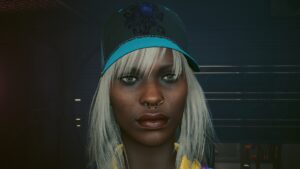 Gesicht einer dunkelhäutige Frau mit Basecap und Ohrringen im Close-Up. Screenshot aus dem Spiel Cyberpunk2077