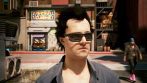 Porträt eines dunkelhaarigen Mannes mit Sonnenbrille und offenem dunklen Hemd in der Stadt Night City bei Sonnenschein. Screenshot aus dem Spiel Cyberpunk2077.