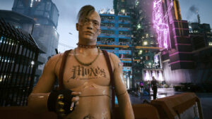 Knapp bekleideter junger Mann mit plastikähnlicher haut und einer moxtätowierung am Rauchen vor dem Nachtclub The Lizzies. Screenshot aus dem Spiel Cyberpunk2077.