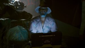 Alter brätiger Mann im Schlapphut, der in dreckigen Kleidern zwischen Müllsäcken im Dunklen Am Laptop sitzt. Screenshot aus dem Spiel Cyberpunk2077.