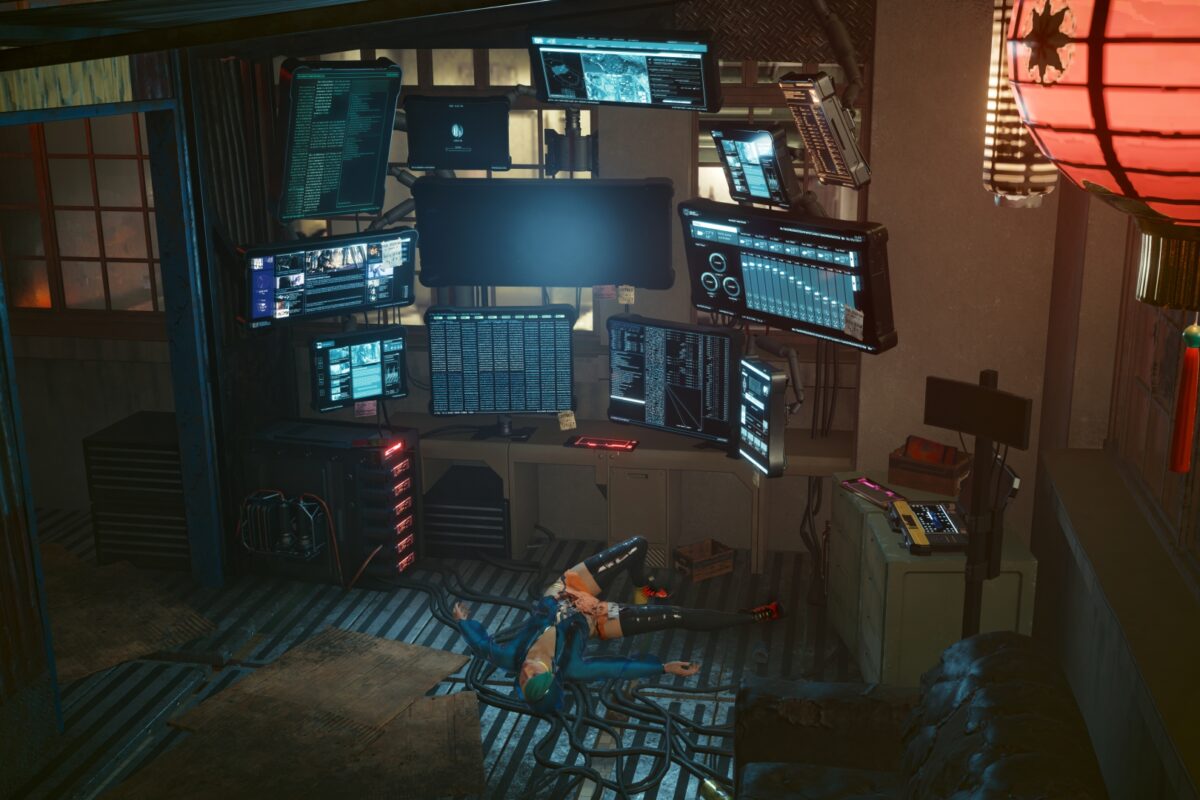 Computeranlage mit mehreren Monitoren in einer Wellblechhütte. Auf dem Boden eine weibliche Leiche. Screenshot aus dem Spiel Cyberpunk 2077.
